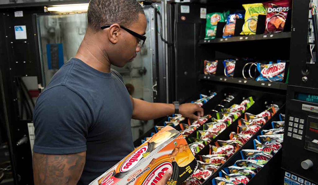 An employee of D&D Delights restocking and servicing a Denver based vending machine with a smile, providing exceptional service for free.